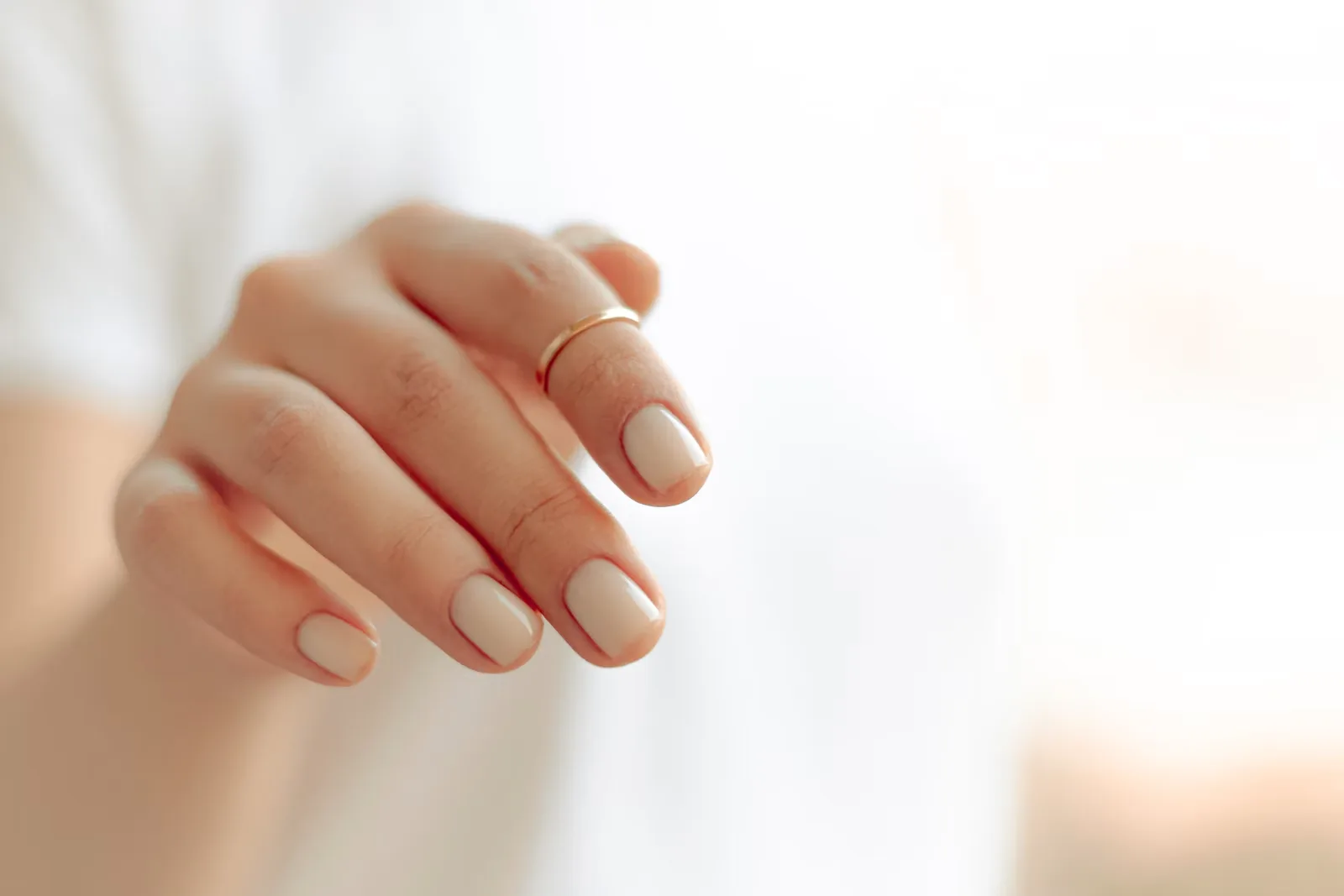 Hand with beige polished nails and a thin gold ring held toward the camera