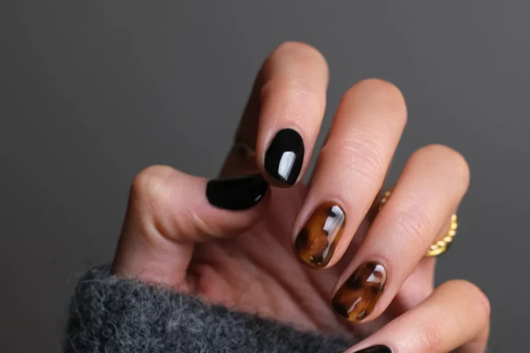 Hand in a grey knit sweater showing short black and tortoiseshell patterned nails