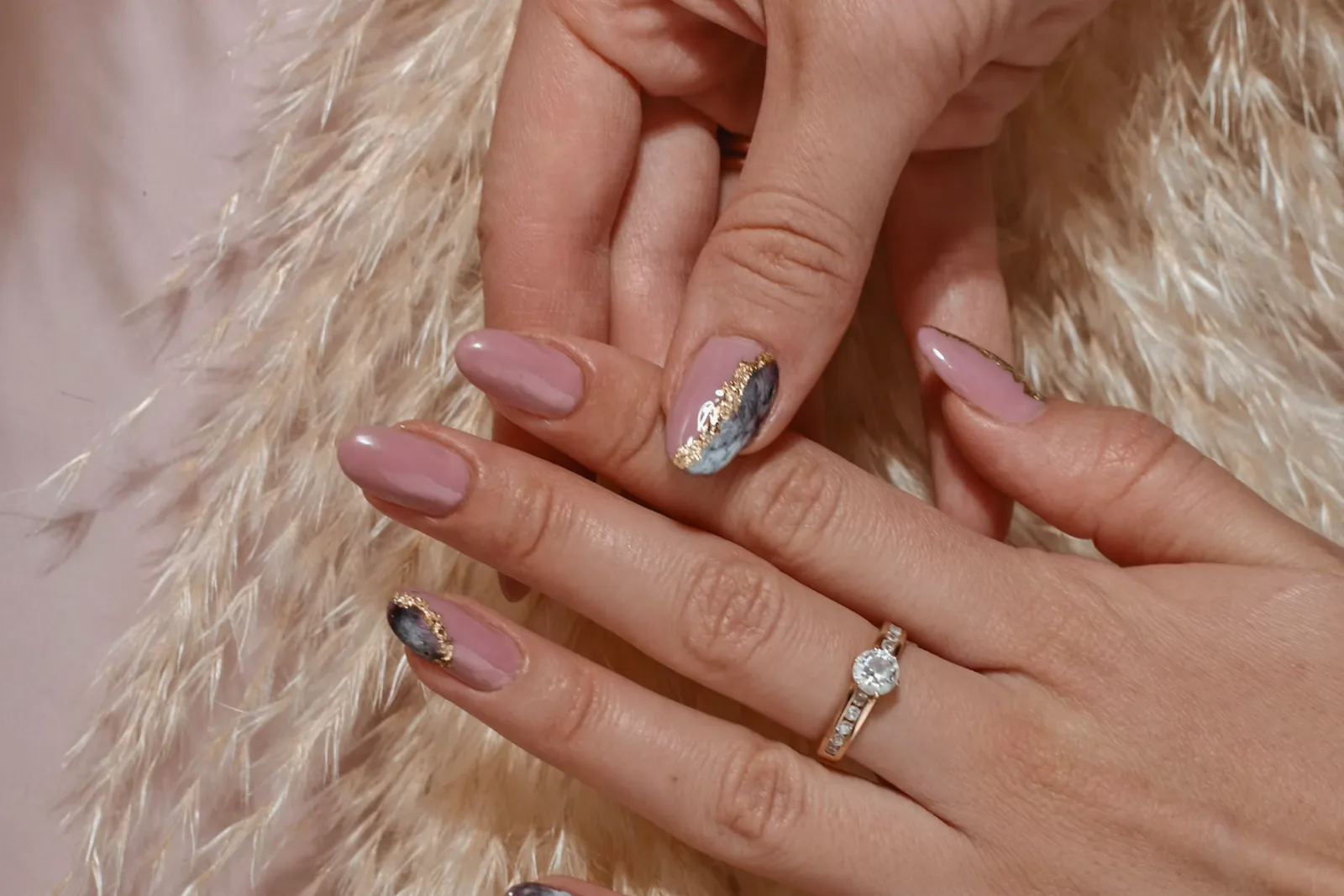 Hands with mauve pink nails, silver accents and a ring against cream pampas grass