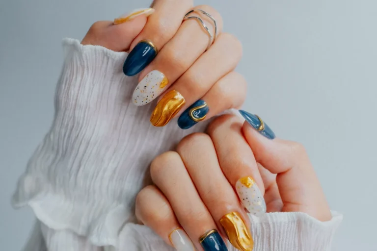 Two hands in white ruffled sleeves showing navy, gold and white nail art