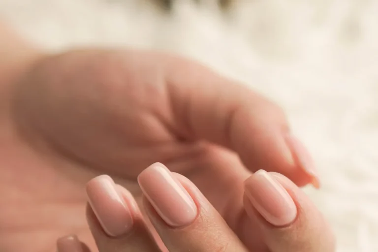 Hand with short square pale pink polished nails resting on a white fur surface
