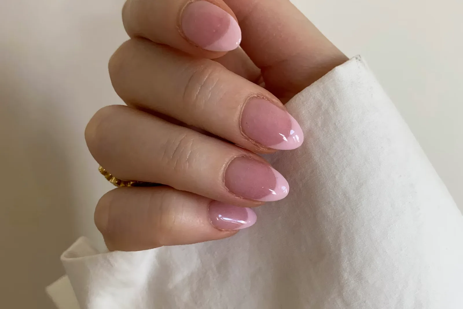 Hand with pale pink almond nails and a thin ring resting on white paper