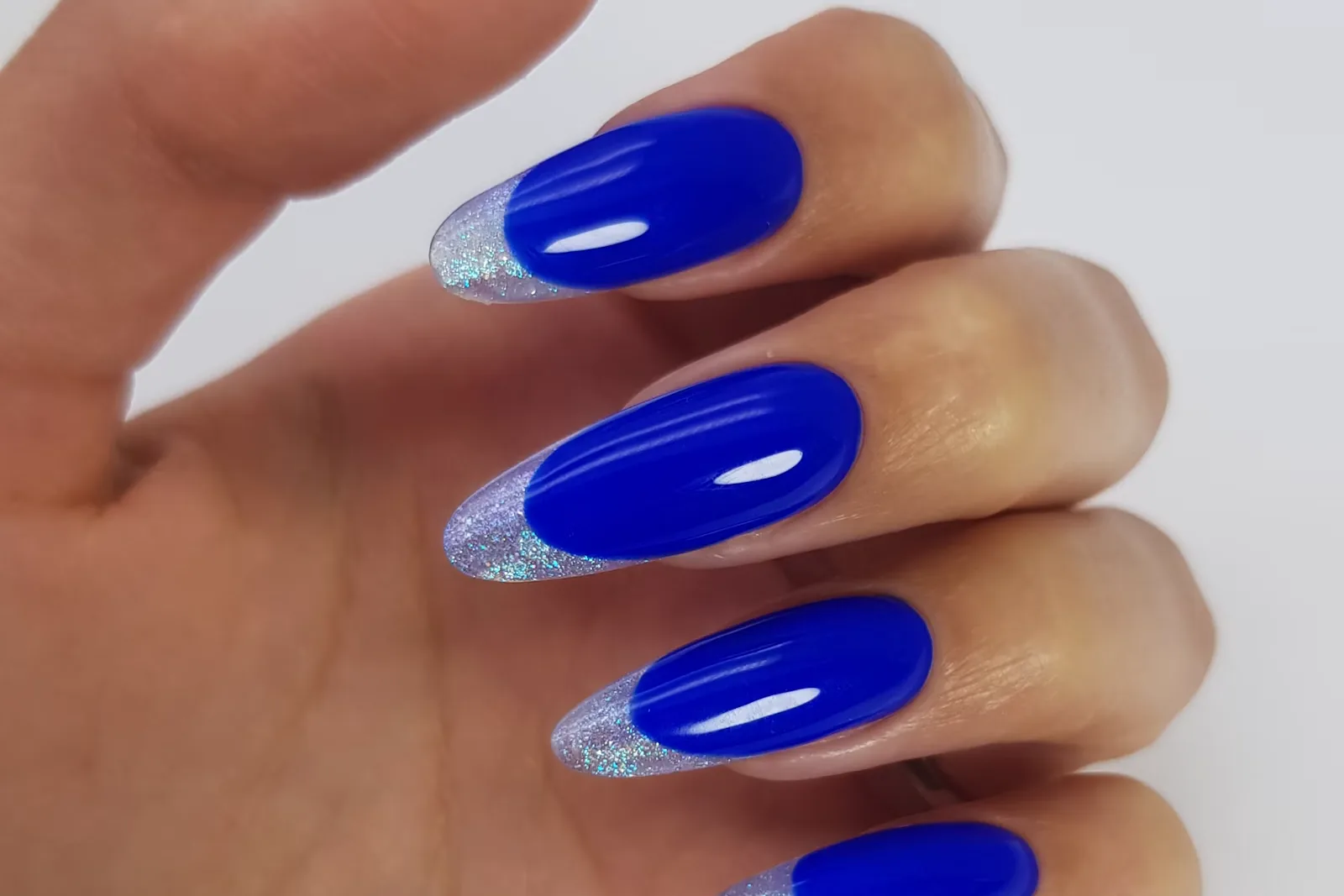 Hand with long royal blue almond nails with silver glitter tips on a white background